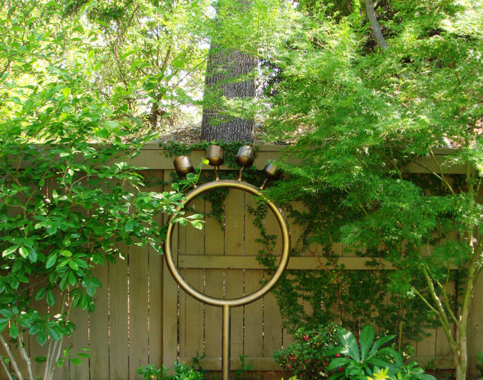 an image of a custom lighting installation that looks like a gold ring with four protruding lights on top of it pointing up at the trees