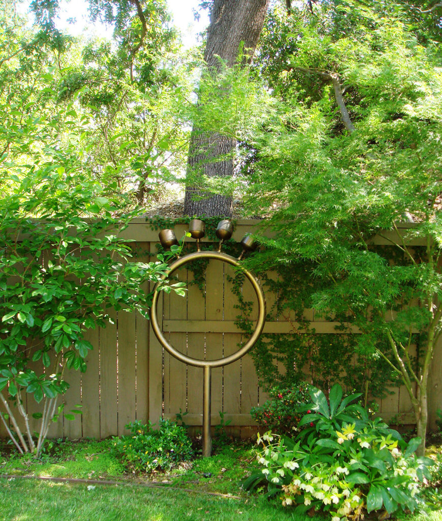 an image of a custom lighting installation that looks like a gold ring with four protruding lights on top of it pointing up at the trees