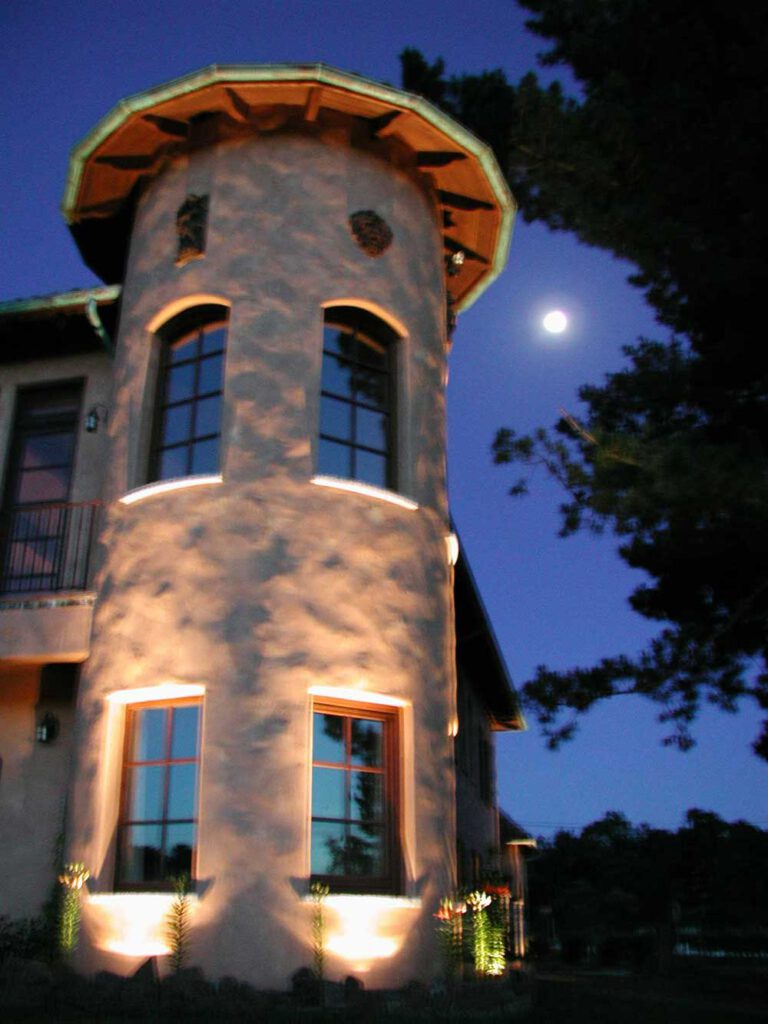 an image of a residential turret lit up at night with the moon in the sky